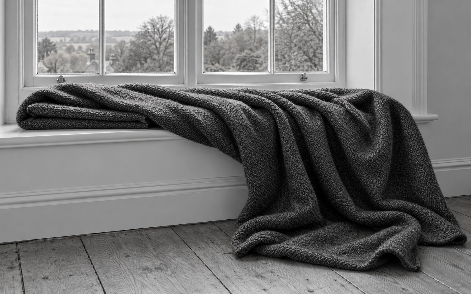 A dark wool blanket lies partly folded on a windowseat and drapes loosely onto the wooden floor.