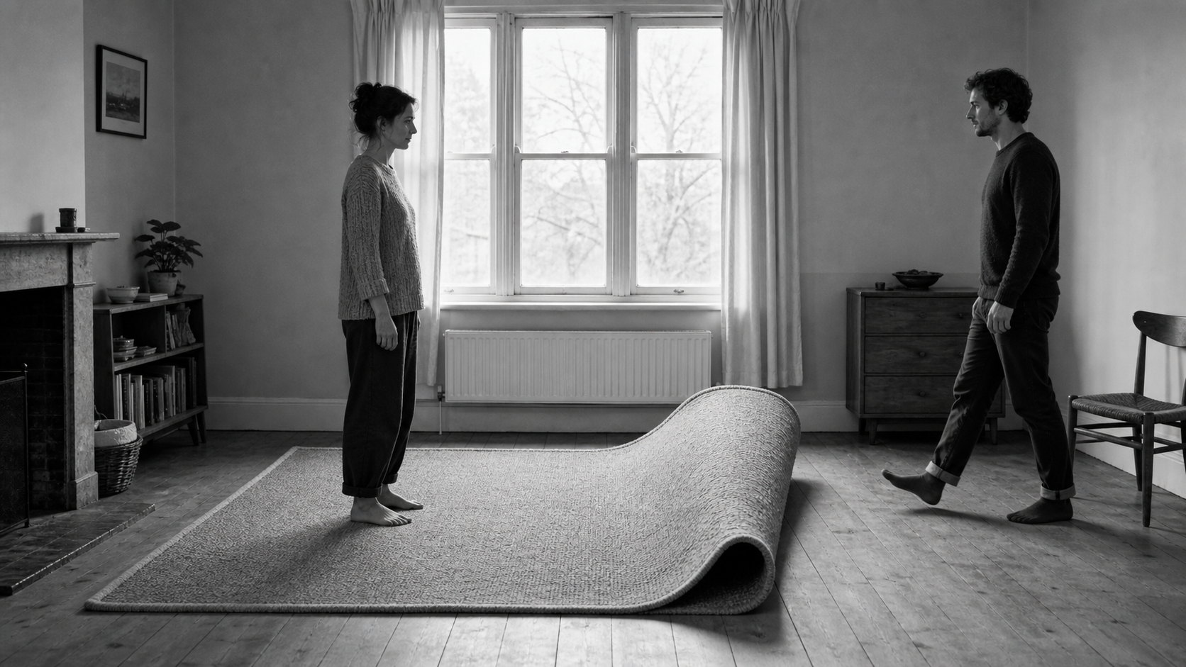 A man crosses a room towards a woman standing still, and the rug between them curls up into a wave that has not yet reached her.