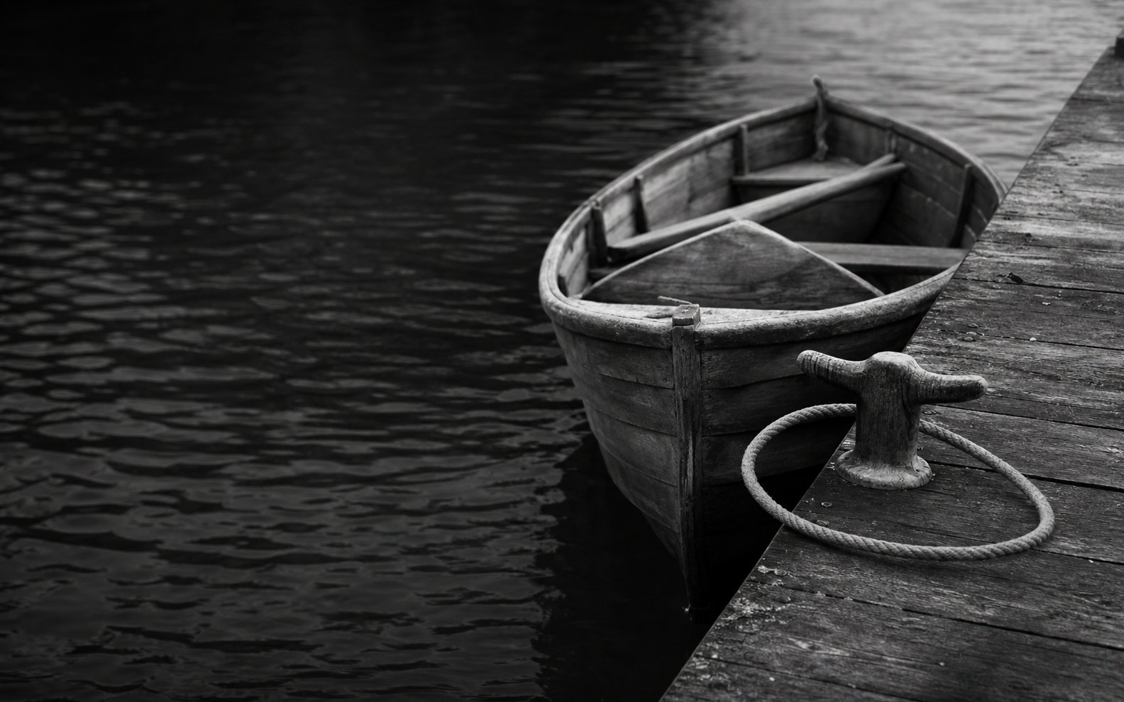 A wooden boat resting alongside a jetty, its rope looped once around the cleat but not tied.