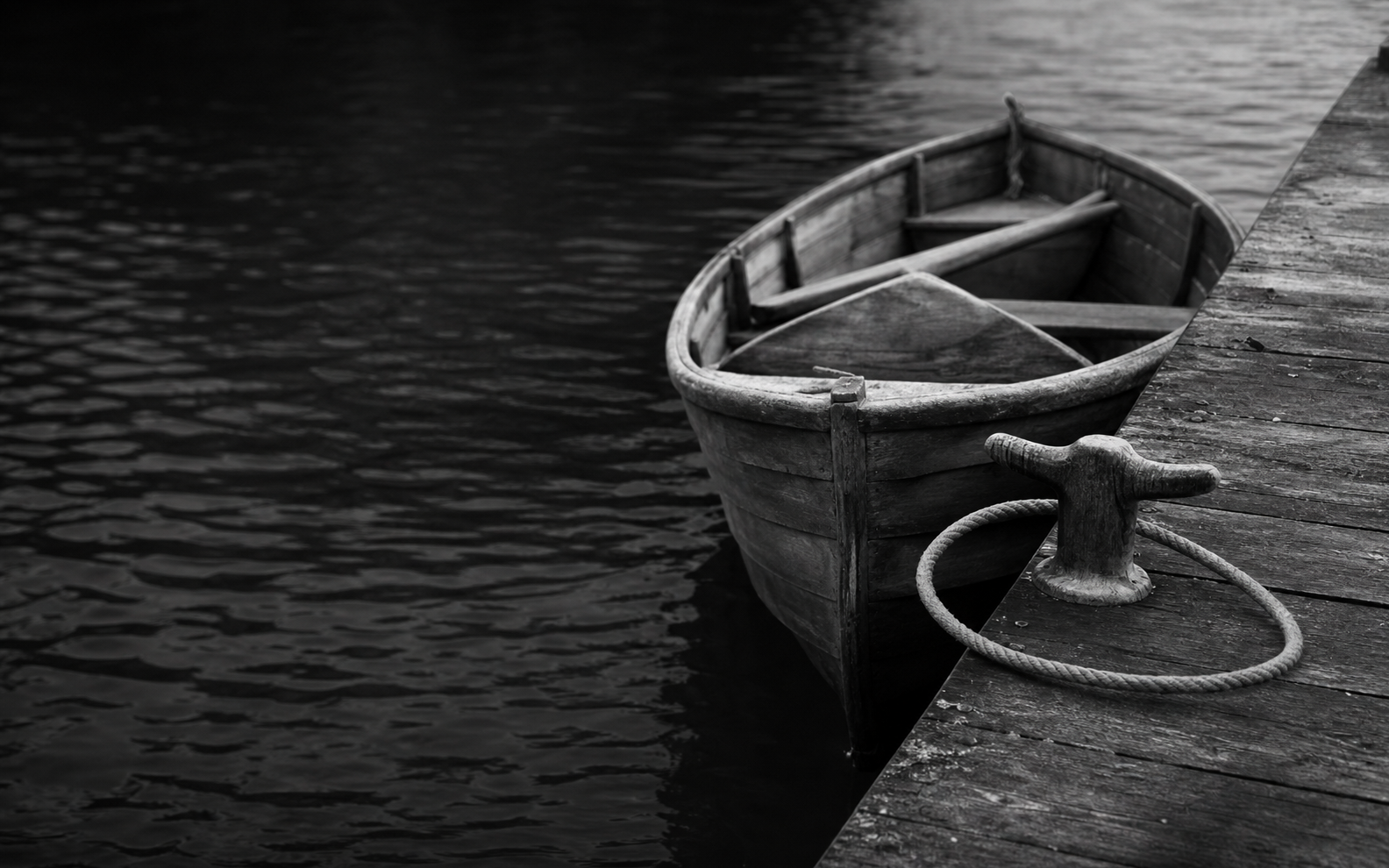A wooden boat resting alongside a jetty, its rope looped once around the cleat but not tied.