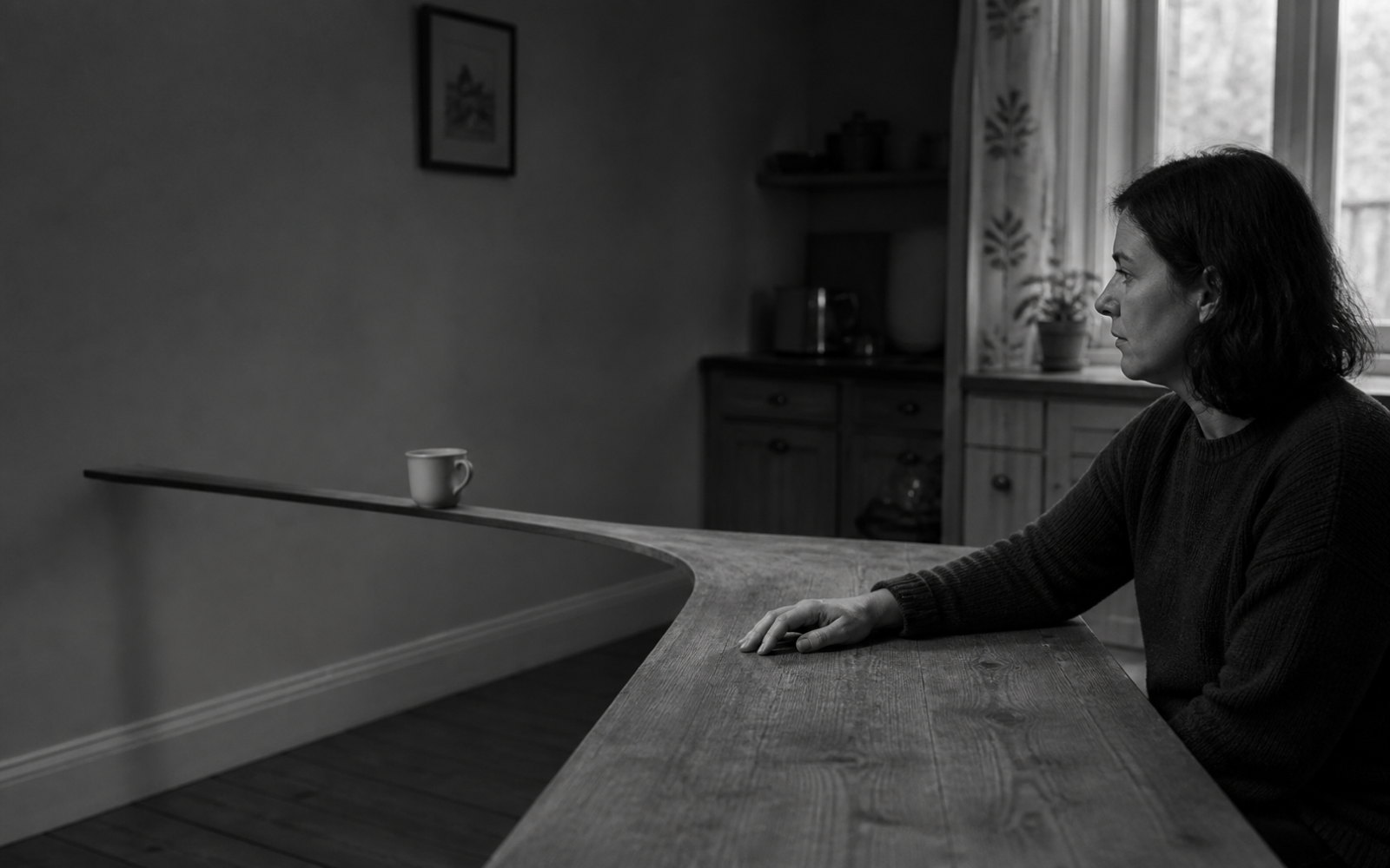 A woman rests her hand on a broad wooden table that narrows into a thin ribbon carrying a mug across the room.