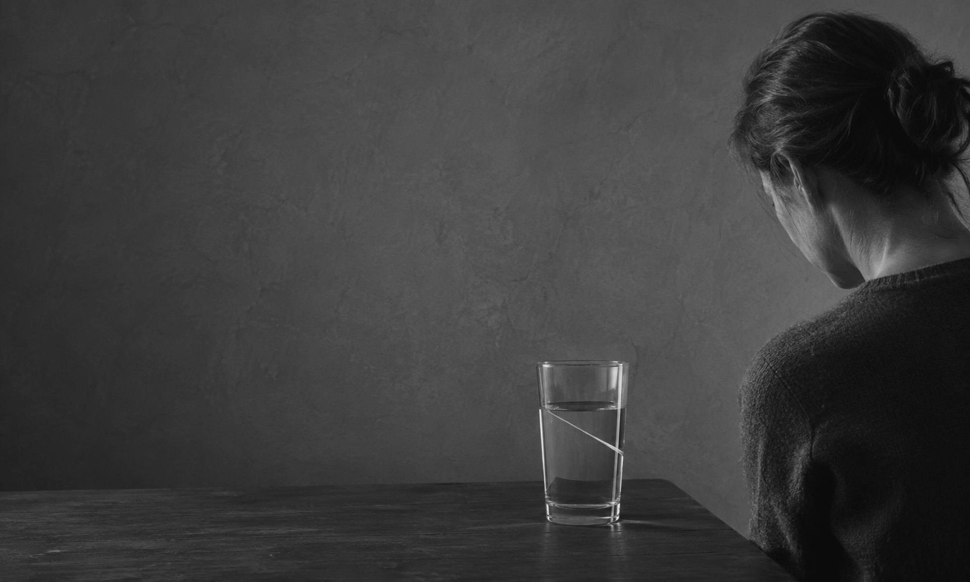 A woman sits at a table before a glass of water in which the surface has set at two different levels at once.