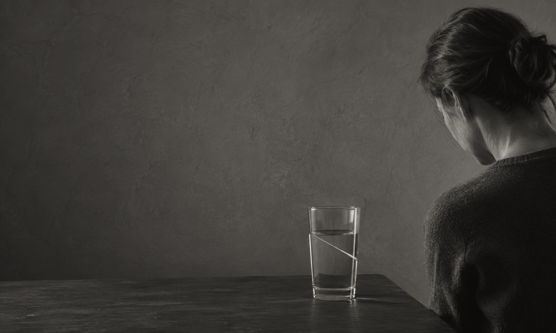 A woman sits at a table before a glass of water in which the surface has set at two different levels at once.