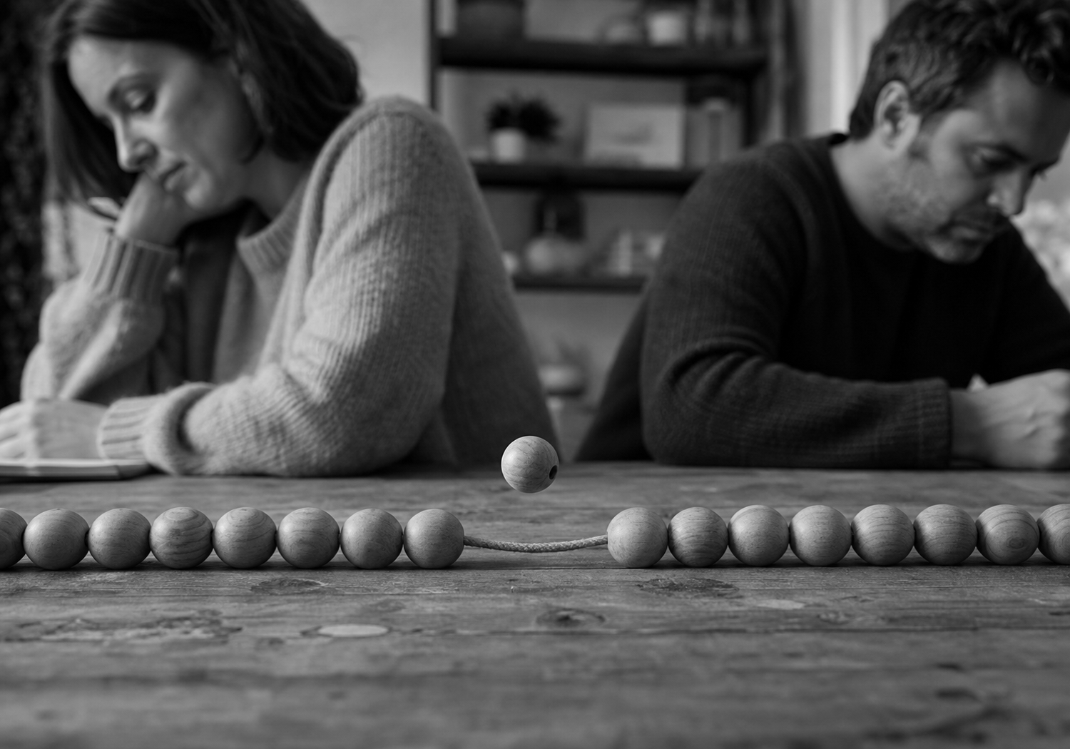 A man and a woman lean on a table from opposite ends, watching a single ball come to rest in a long line of identical balls.
