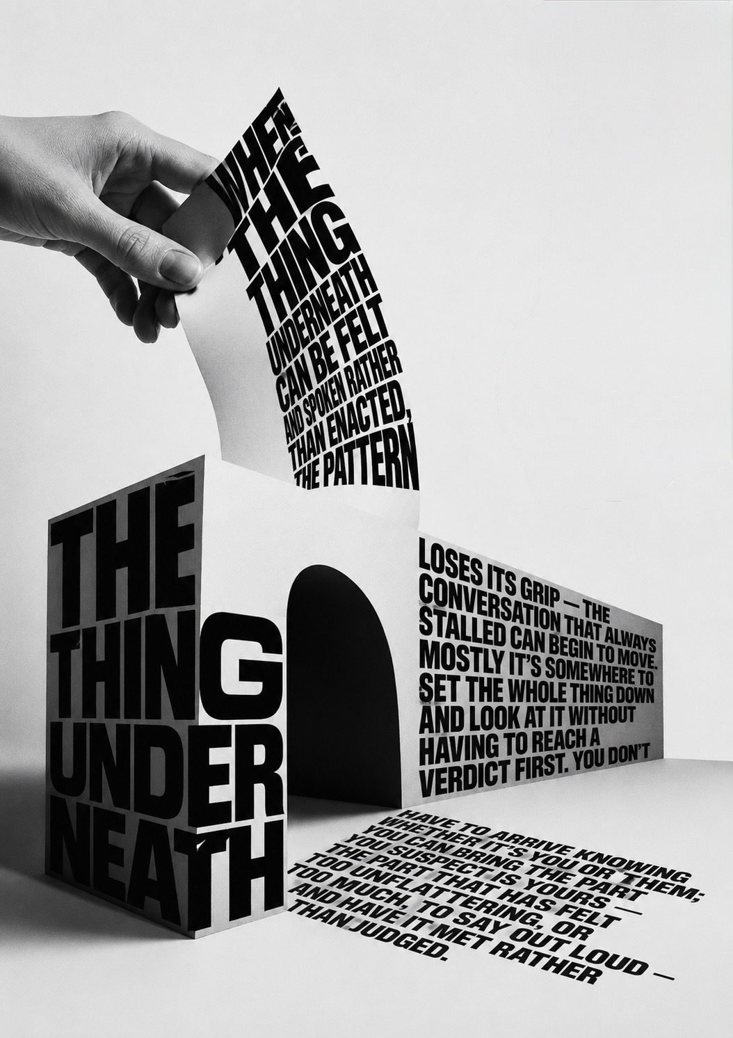 A hand peeling up a curling ribbon of type reading ‘when the thing underneath can be felt and spoken rather than enacted, the pattern’ from a monumental block spelling ‘the thing underneath’, its continuation running across the floor.