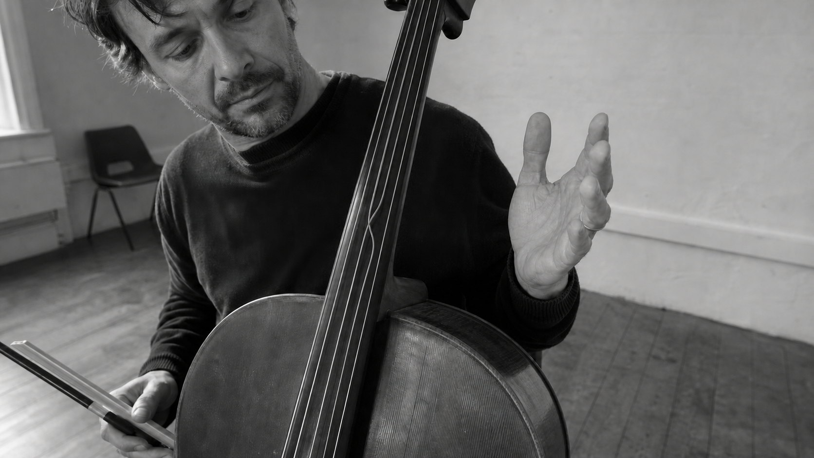 A cellist plays with one hand while the other lifts away from the strings, held open in the air.