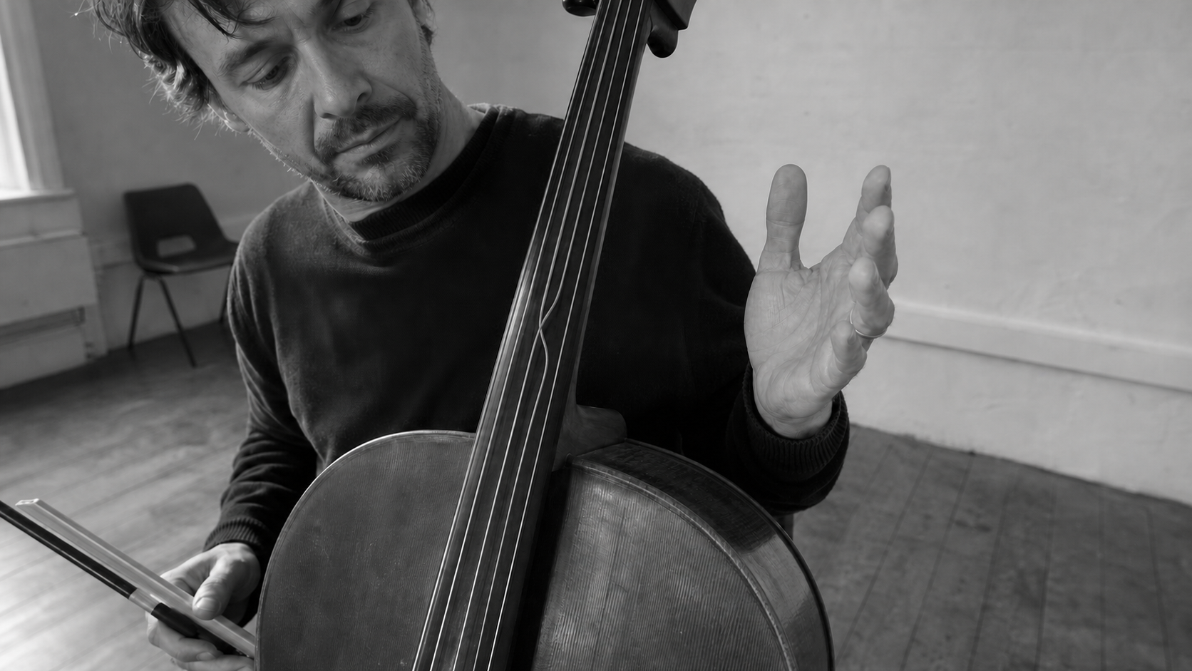 A cellist plays with one hand while the other lifts away from the strings, held open in the air.