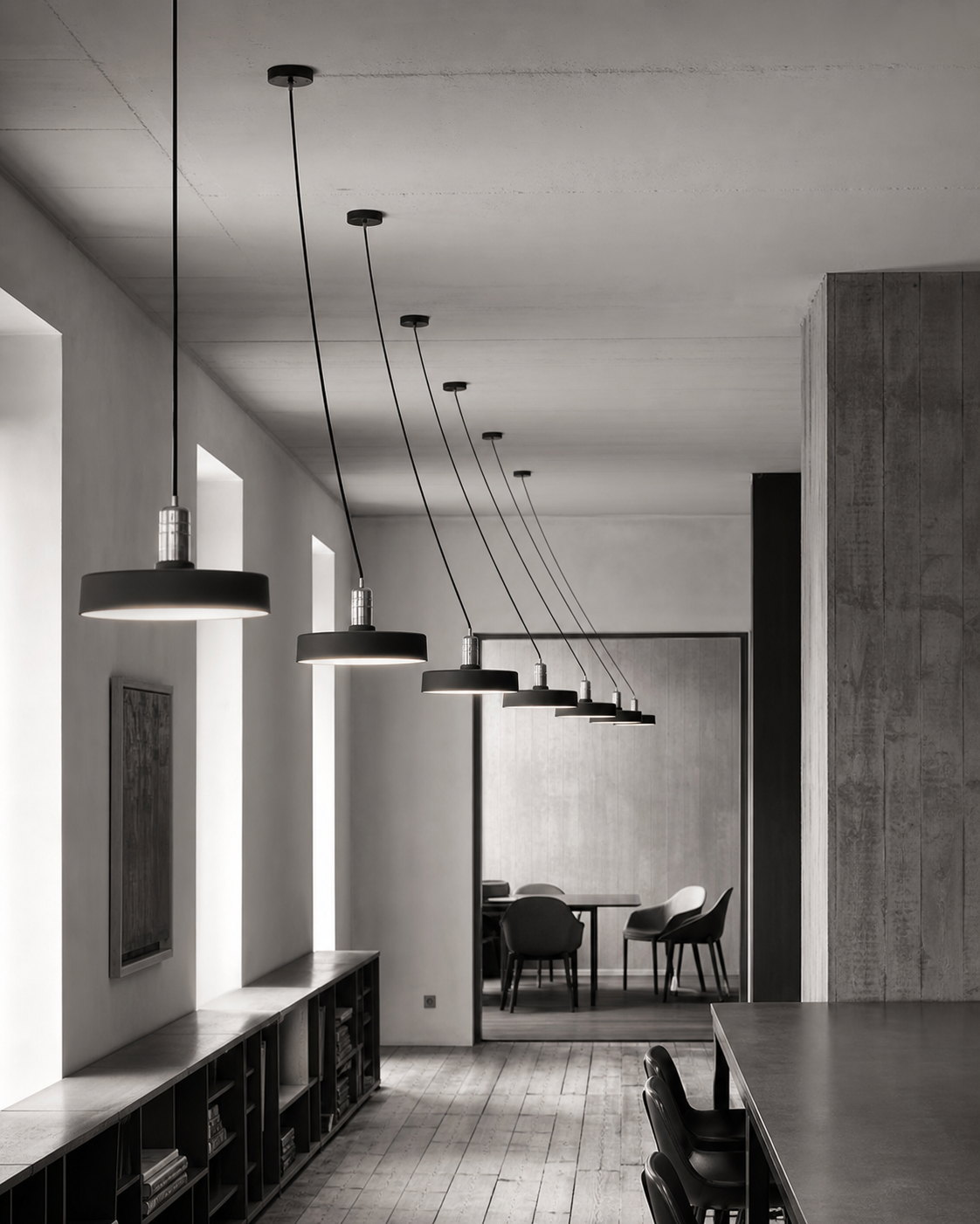 A corridor of pendant lamps receding toward a quiet meeting room, each one lit.