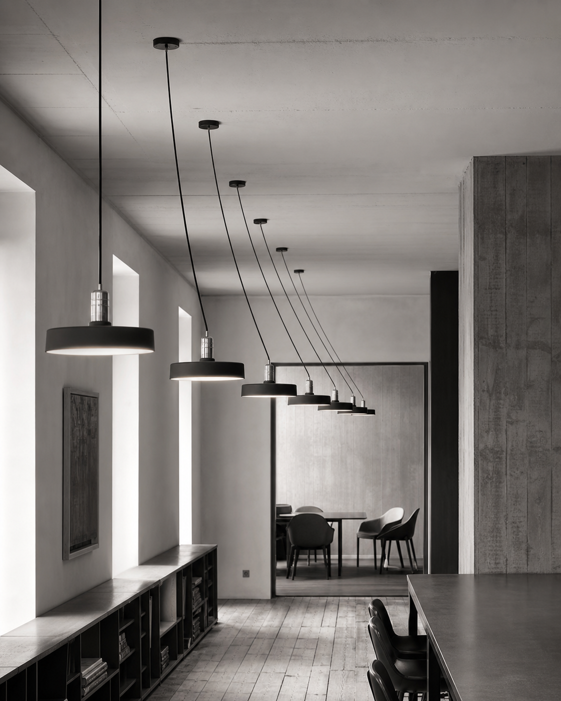 A corridor of pendant lamps receding toward a quiet meeting room, each one lit.