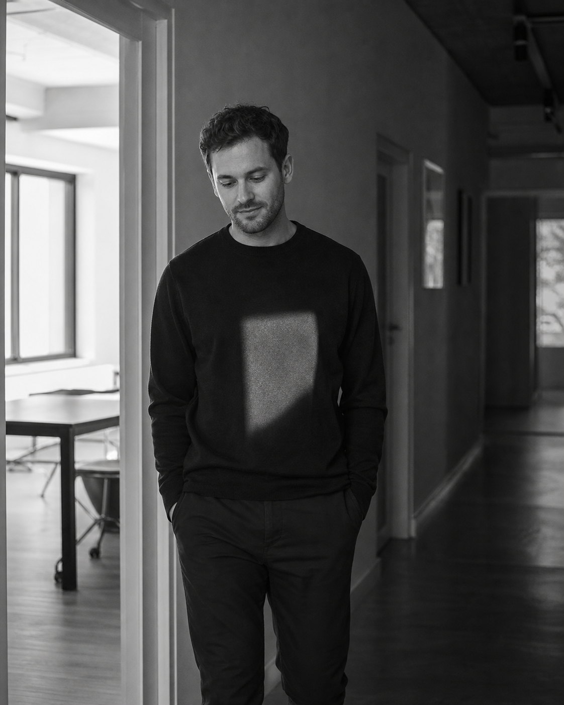 A man standing in a doorway, a square of daylight resting on him, hands in pockets, unhurried.