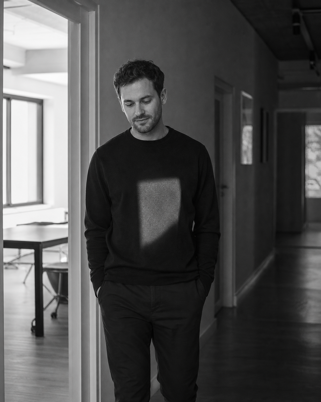 A man standing in a doorway, a square of daylight resting on him, hands in pockets, unhurried.