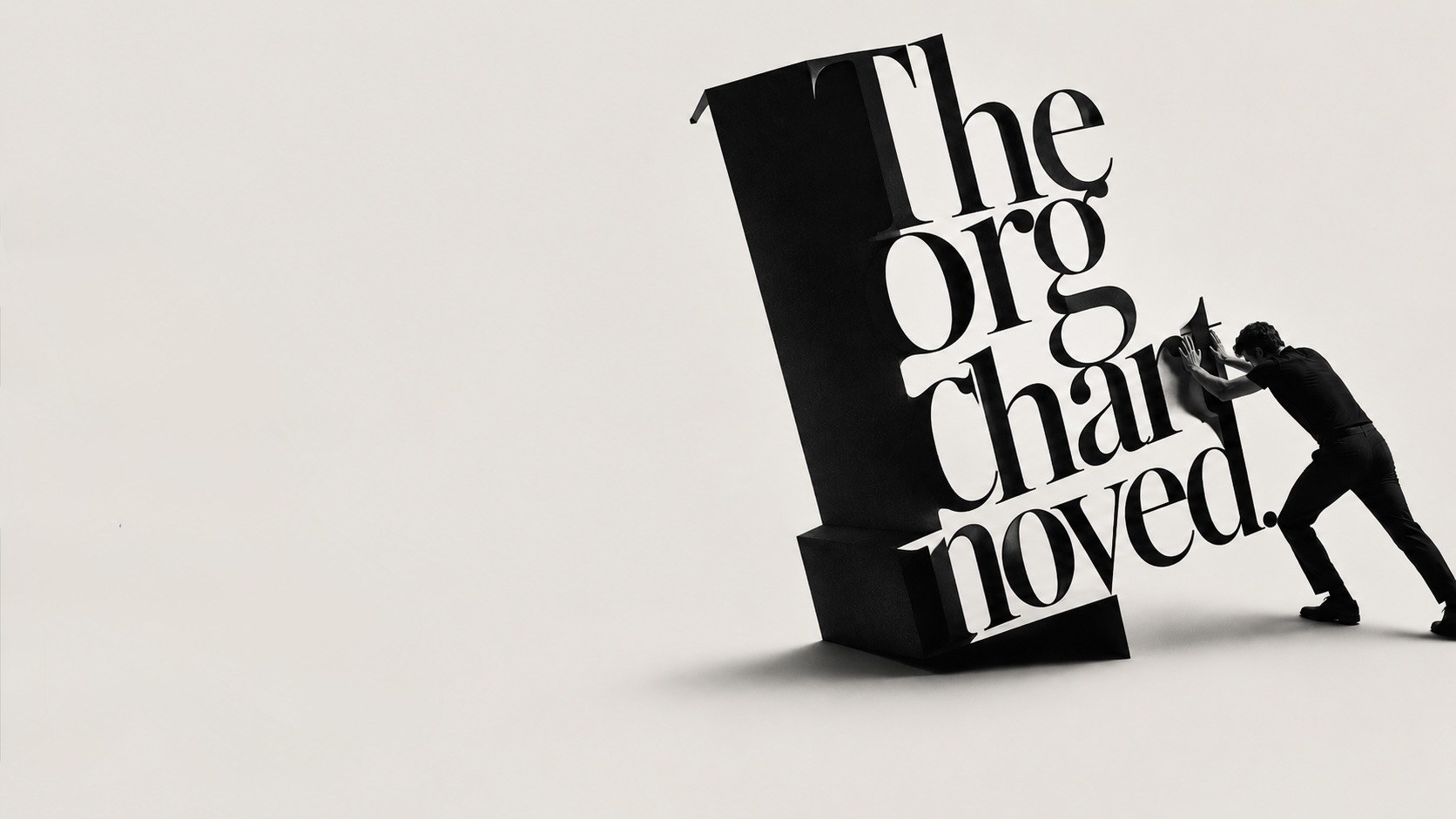 A man bracing to push the toppling three-dimensional words &lsquo;The Org Chart moved.&rsquo; upright, a wide expanse of pale wall to the left.