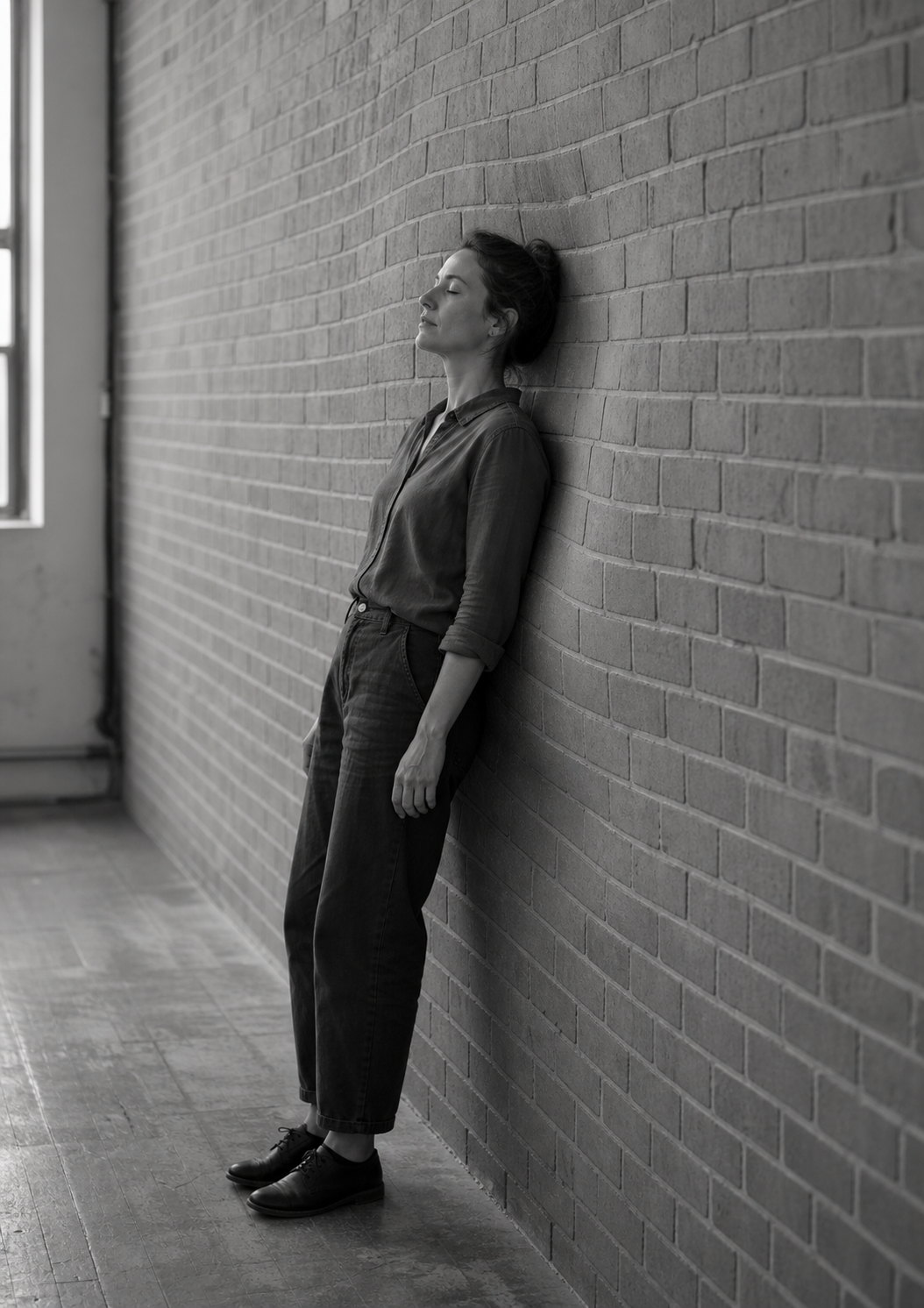 A woman stands with her back flat against a brick corridor wall, holding still in a passage with nowhere to sit.