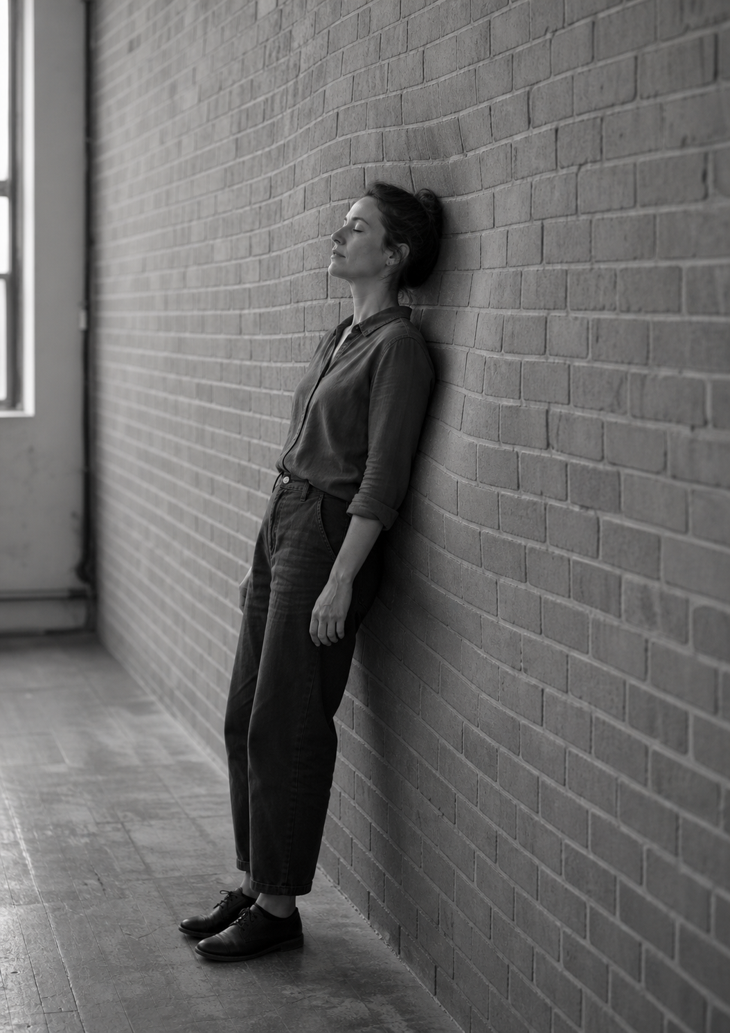A woman stands with her back flat against a brick corridor wall, holding still in a passage with nowhere to sit.